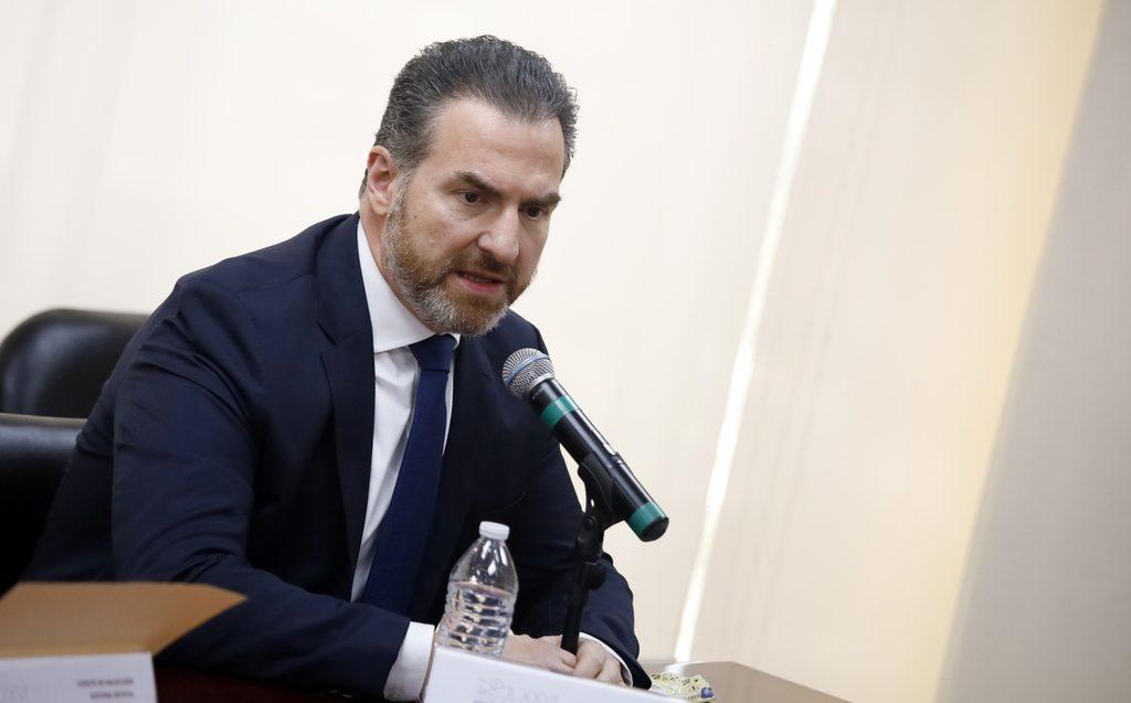 COMPARECENCIA FISCAL - HECHOS AM Man in a dark suit and blue tie speaking into a microphone at a panel, with a water bottle on the table in front of him.