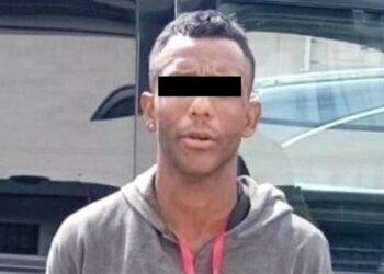 Man with short dark hair wearing a gray hoodie; eyes obscured by a black bar to anonymize identity.