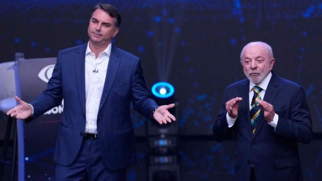 hechos-am-se-insultan-lula-bolsonarojpg - HECHOS AM Two men in suits on a stage, one extending his arms while the other gesticulates, likely hosts during a talk show or presentation.